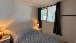 A bedroom with a bed, bedside lamps, a window with curtains, a small table, and a wall-mounted shelf. - One-bedroom apartment with terrace, AC and parking in Capbreton (Capbreton)