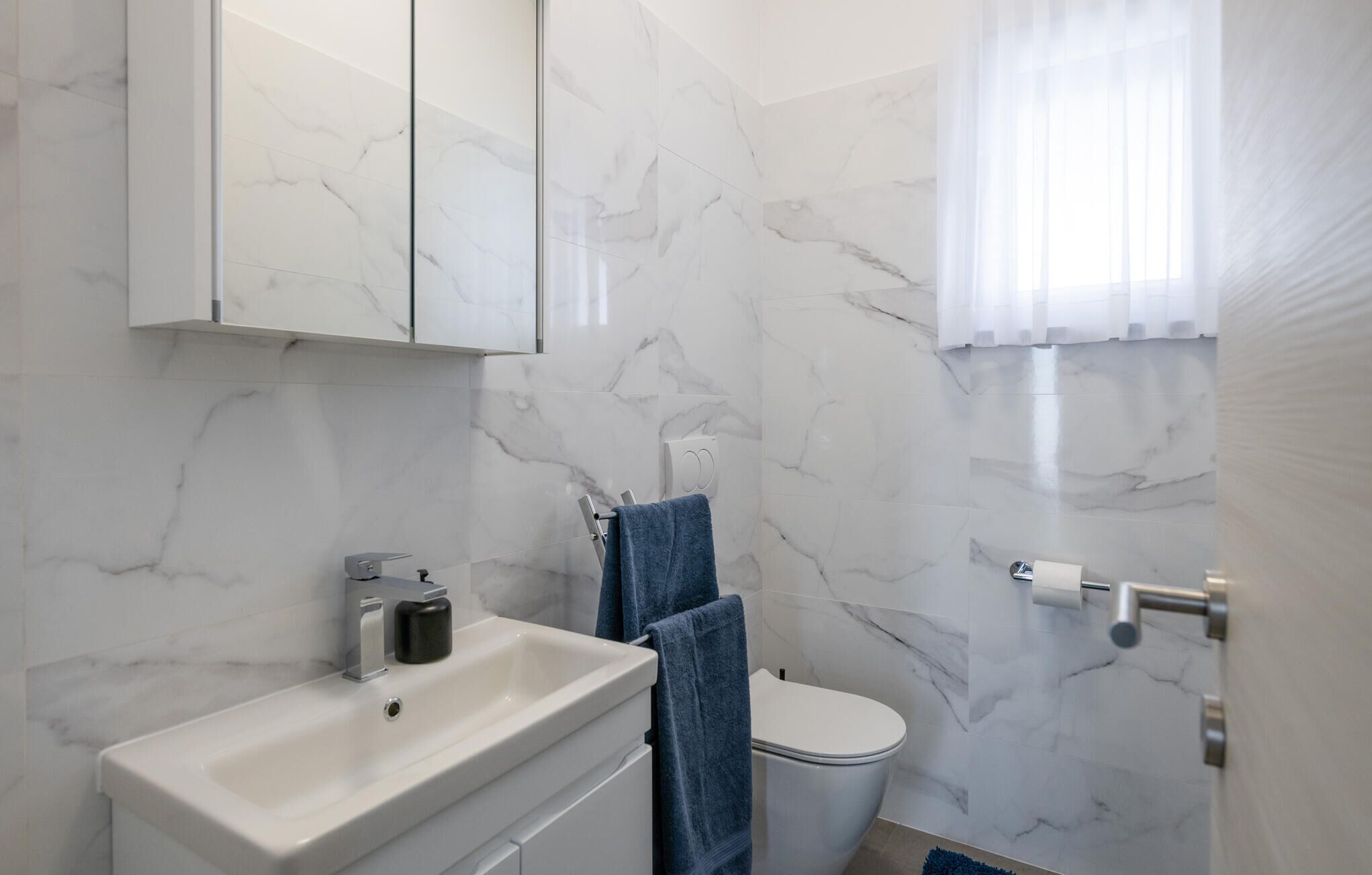 A bathroom with a marble wall, a white sink, a toilet, and a blue towel.