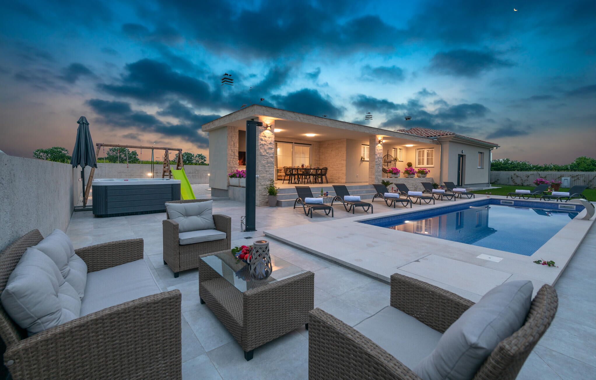 A modern outdoor pool area with lounge chairs, a hot tub, and a dining area.