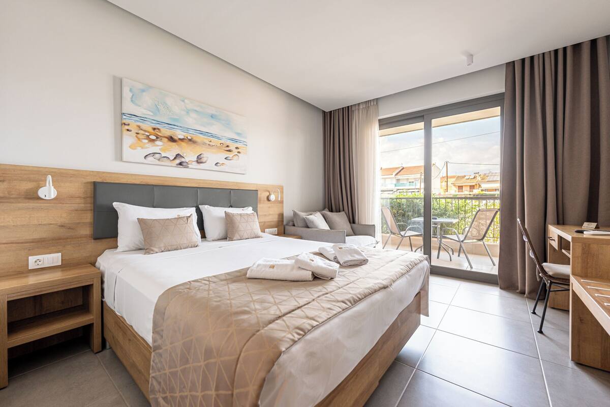 Habitación de hotel con una cama grande, un escritorio, una silla, un balcón con vistas y un cuadro en la pared.
