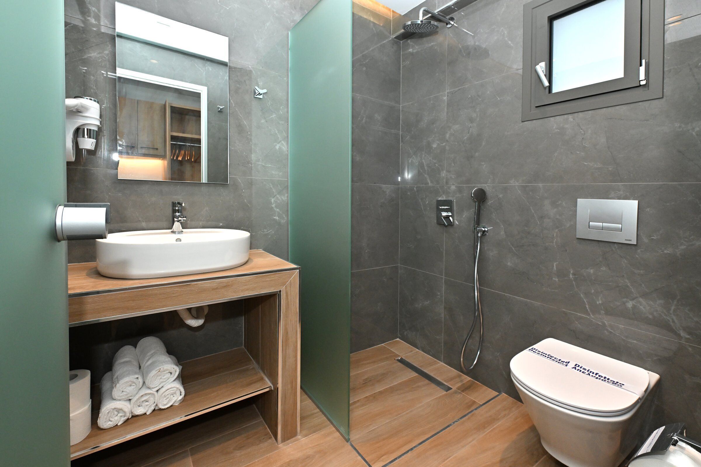 Un baño moderno con lavamanos, espejo, toallero, ducha e inodoro.