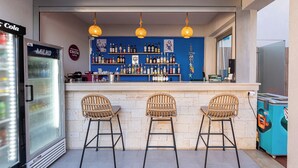 Una zona de bar con mostrador, tres sillas de mimbre, un refrigerador y estantes con botellas.