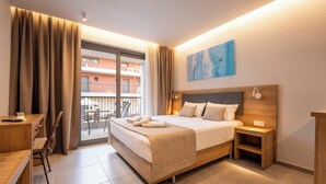 Habitación de hotel con cama, mesita de noche, silla, escritorio y vistas al balcón exterior.