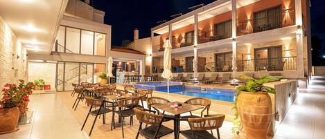 A modern hotel with a pool, outdoor seating, and a well-lit terrace.