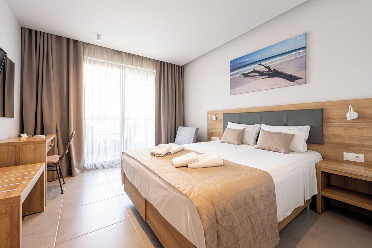 Habitación de hotel con cama, escritorio, silla, televisor y un cuadro de una playa.