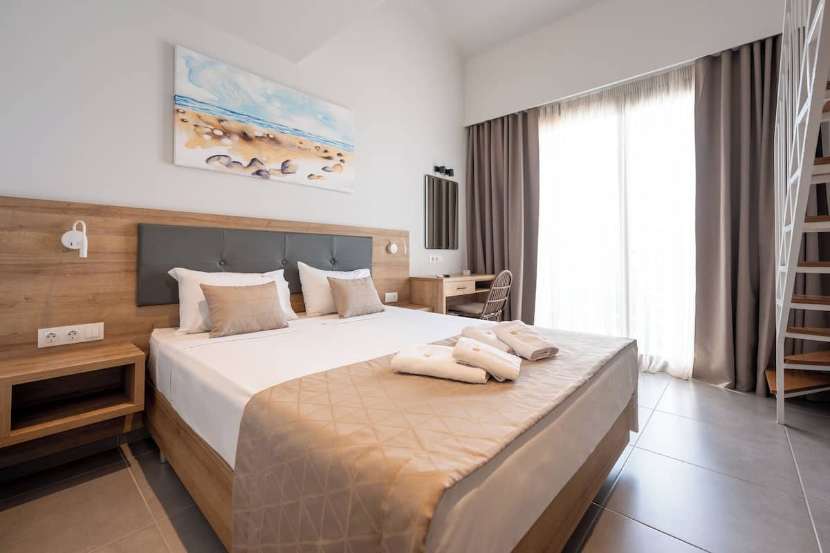 Habitación de hotel con una cama grande, un escritorio, una silla, un cuadro y una ventana con cortinas.