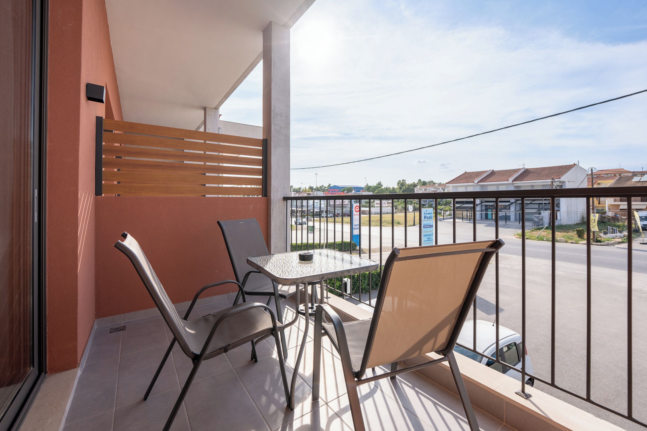 Un balcon avec une table et des chaises, donnant sur un parking et avec des bâtiments en arrière-plan.