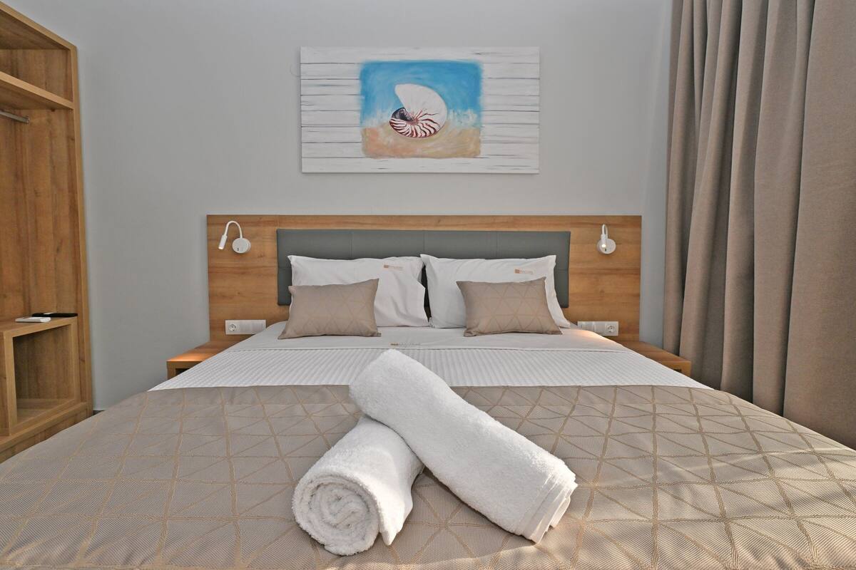 Una cama bien tendida con una colcha de estampado geométrico, dos almohadas y una toalla blanca enrollada sobre la cama.