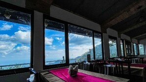 A restaurant with large windows offering a view of the sea and mountains. - Stoneshed Resort And Hotel (Nainital)