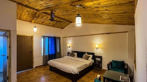A bedroom with a wooden ceiling, a bed with pillows, bedside lamps, and a small table with a chair. - Stoneshed Resort And Hotel (Nainital)