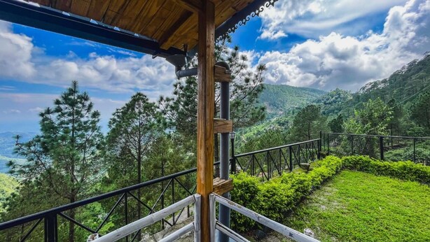A wooden balcony with a metal railing overlooking a lush green landscape and a mountainous backdrop. - Stoneshed Resort And Hotel (Nainital)