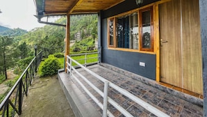 A wooden balcony with a stone floor, a wooden door, and a window with a view of a green landscape. - Stoneshed Resort And Hotel (Nainital)
