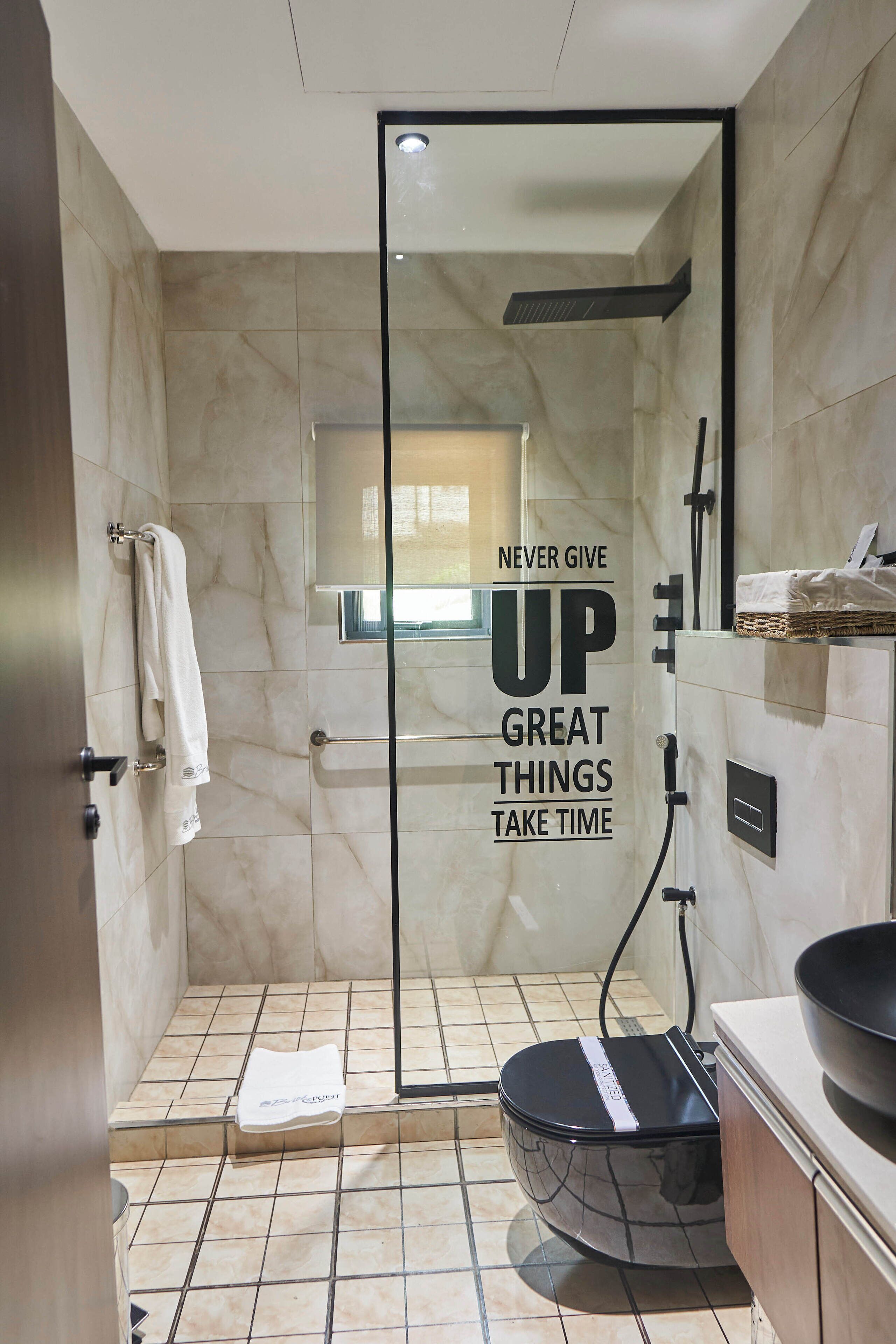 Un bagno moderno con cabina doccia in vetro, un appendi asciugamani e una citazione motivazionale ben visibile sulla parete.
