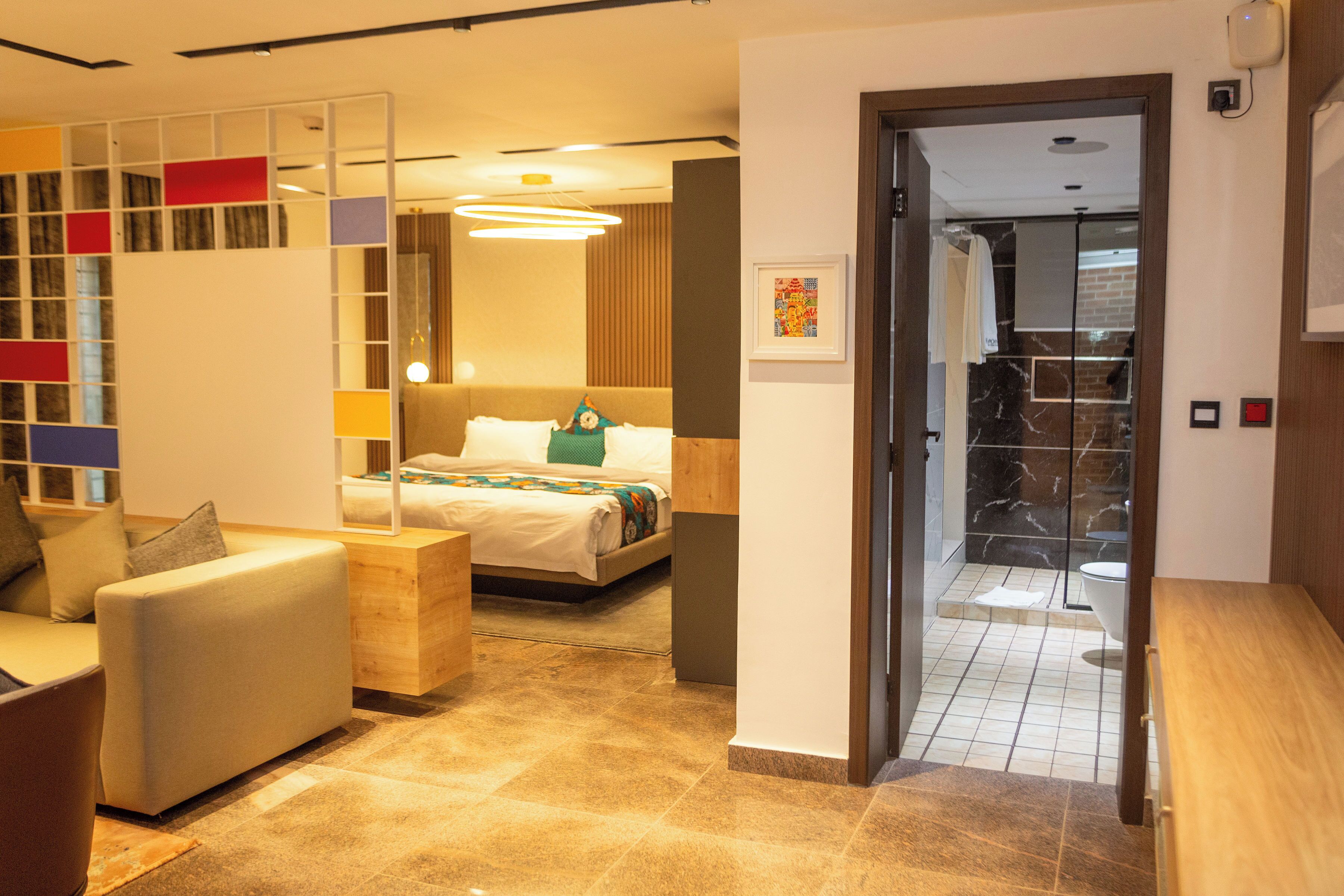 A modern hotel room with a bed, a sofa, a wooden side table, and a bathroom visible through an open door.