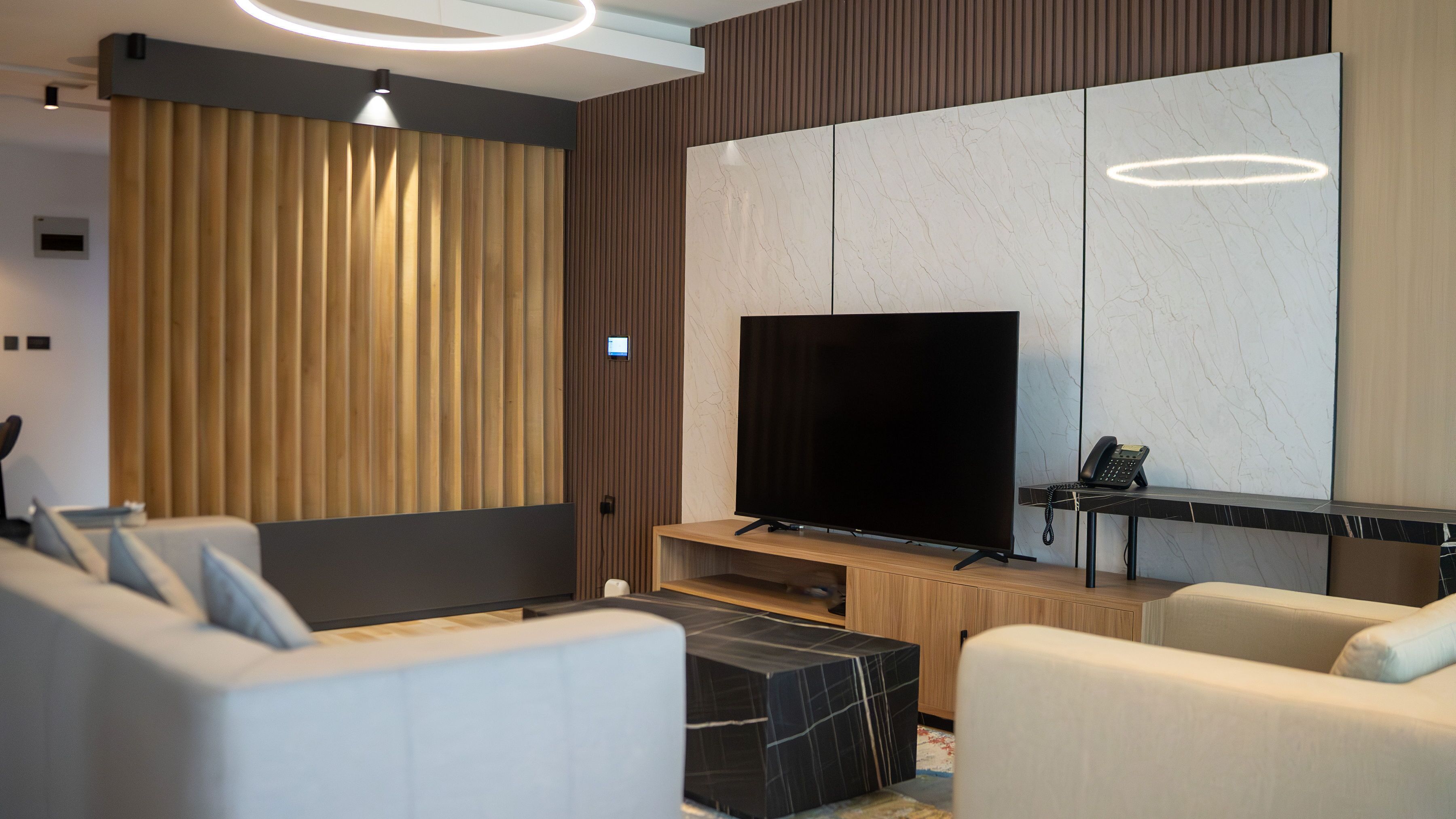 Una sala de estar moderna con un televisor de pantalla plana grande, un sofá, una mesa de centro y una lámpara decorativa.