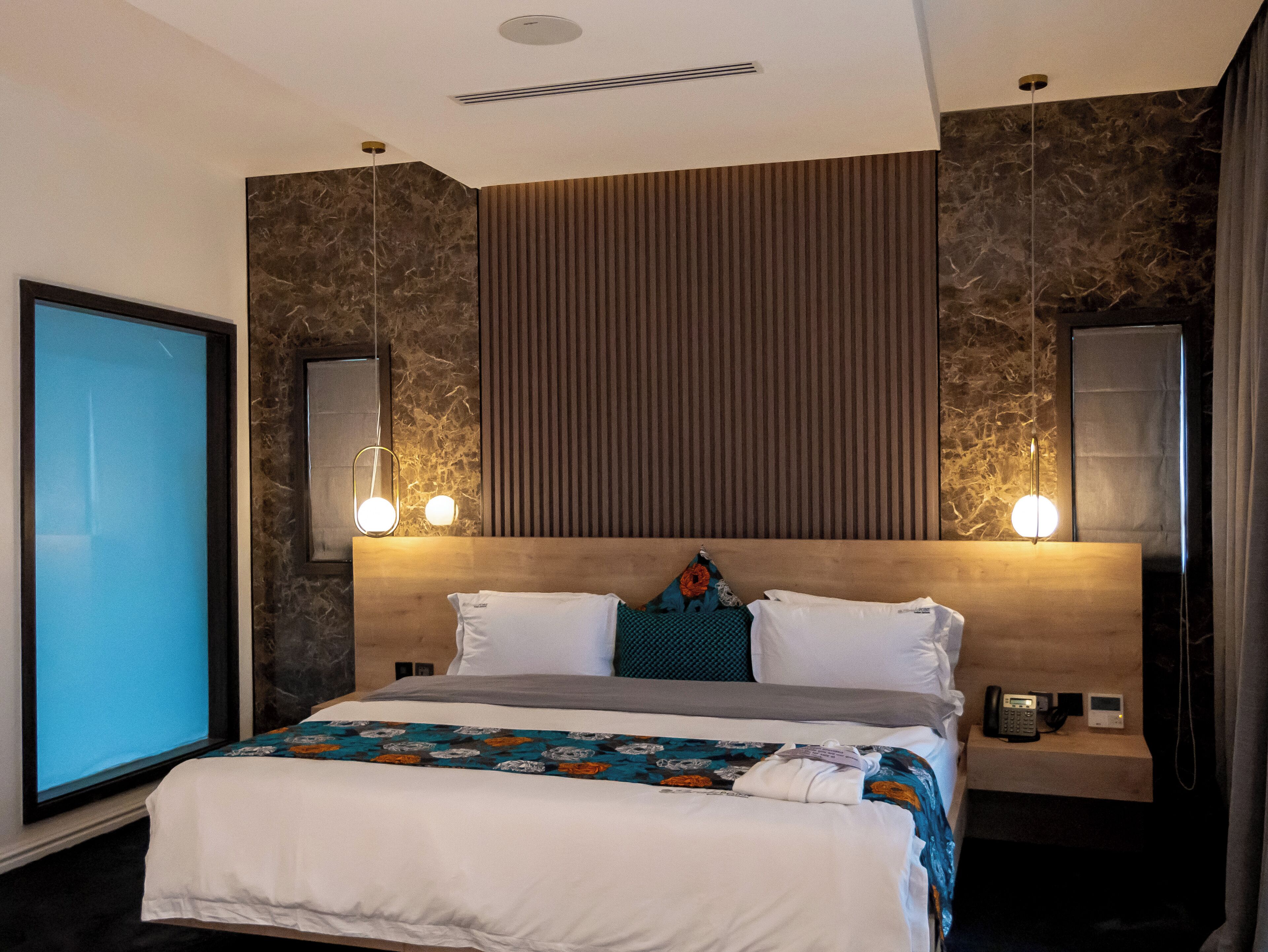Une chambre d’hôtel moderne avec un grand lit, une table de chevet avec un téléphone et une petite enceinte, et un grand miroir au mur.