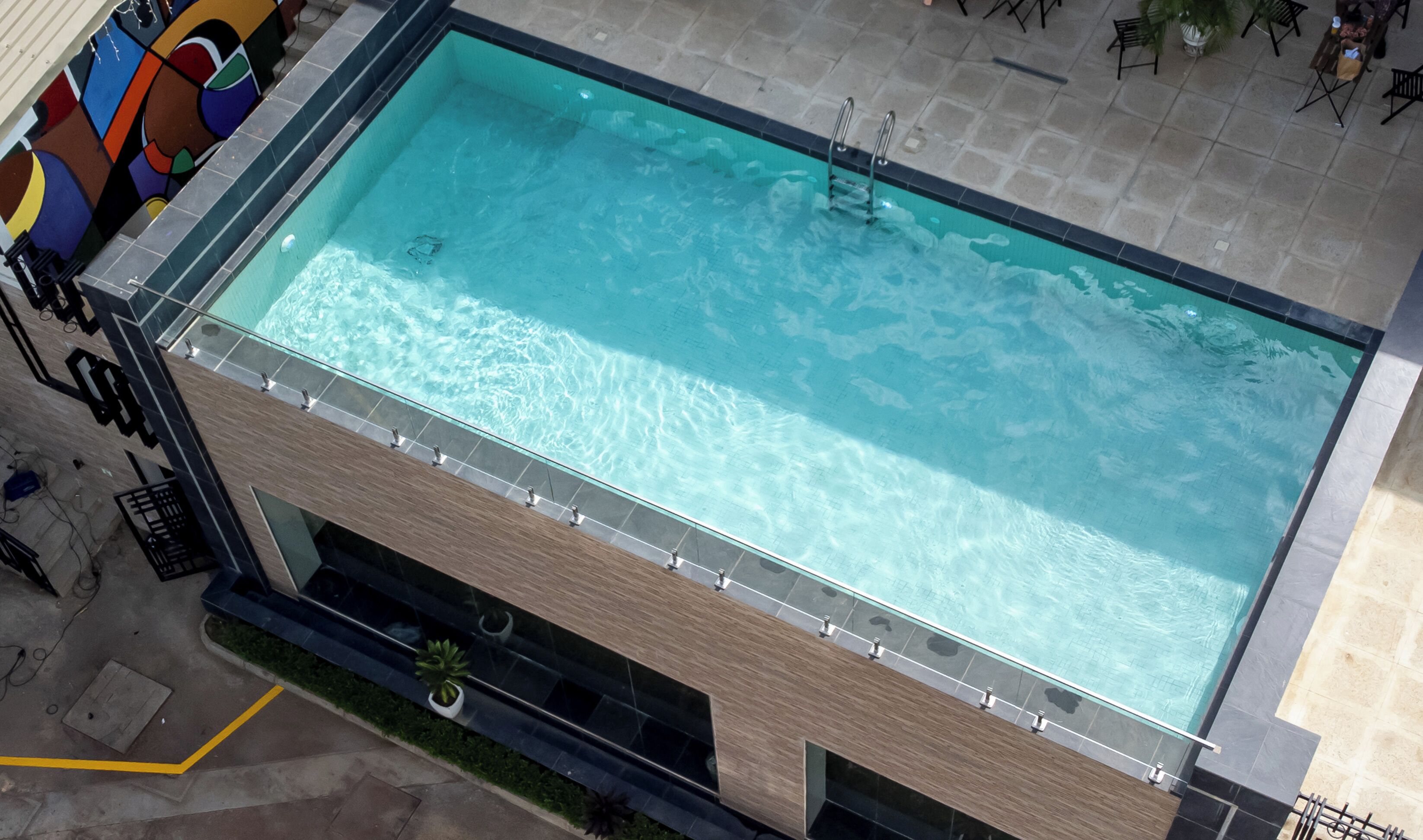 A rectangular swimming pool with clear water, surrounded by a tiled deck and a modern building facade.