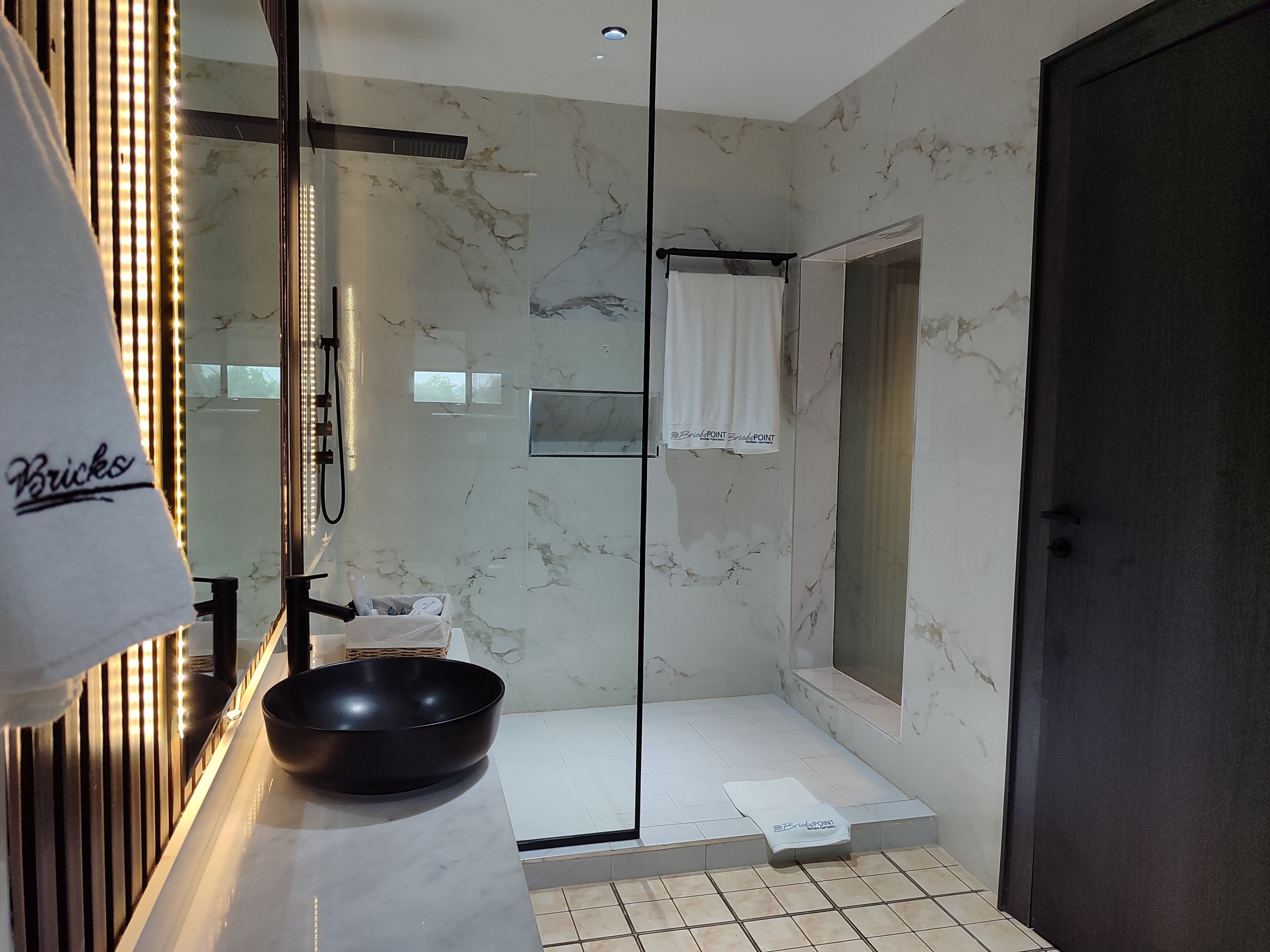 A modern bathroom with a marble wall, a black basin, a towel rack, and a glass shower enclosure.