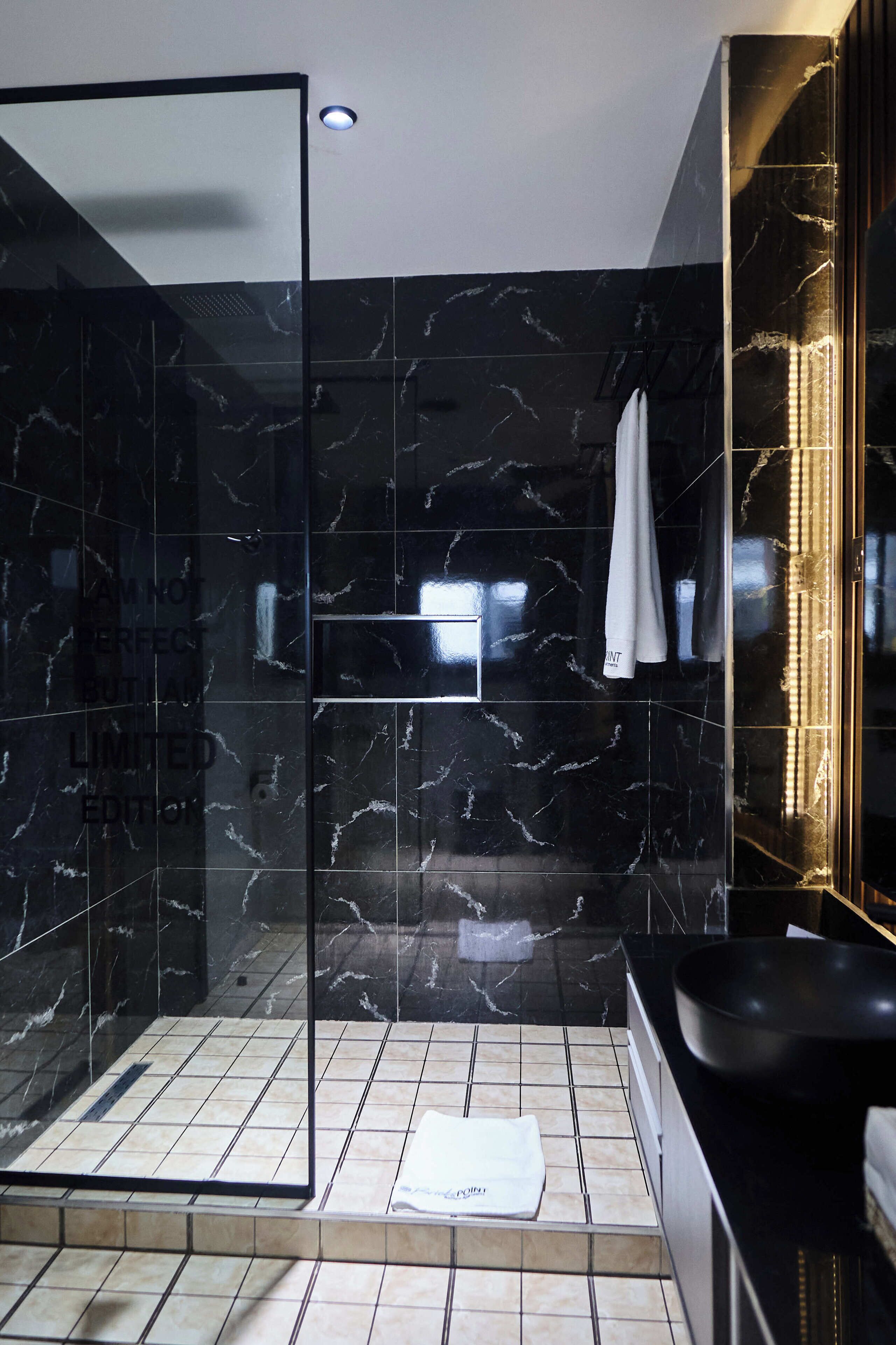 A modern bathroom with a glass-enclosed shower, black marble walls, and a black sink.