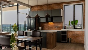 A modern kitchen with a large island, pendant lights, and a view of the city through a large window. - BRICKSPOINT BOUTIQUE APARTHOTEL ASOKORO (Abuja)