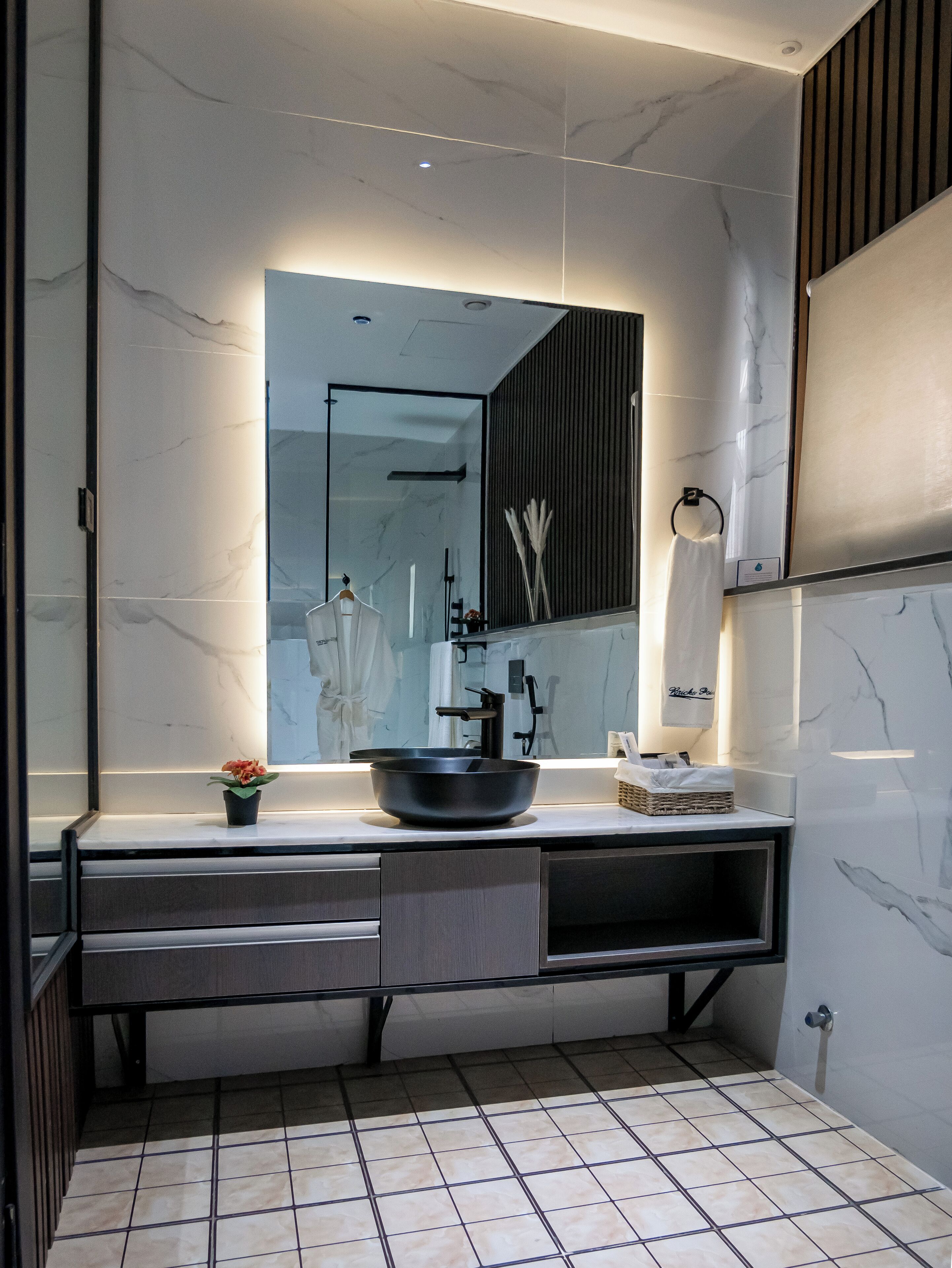 A modern bathroom with a large mirror, a black vessel sink, and a potted plant.