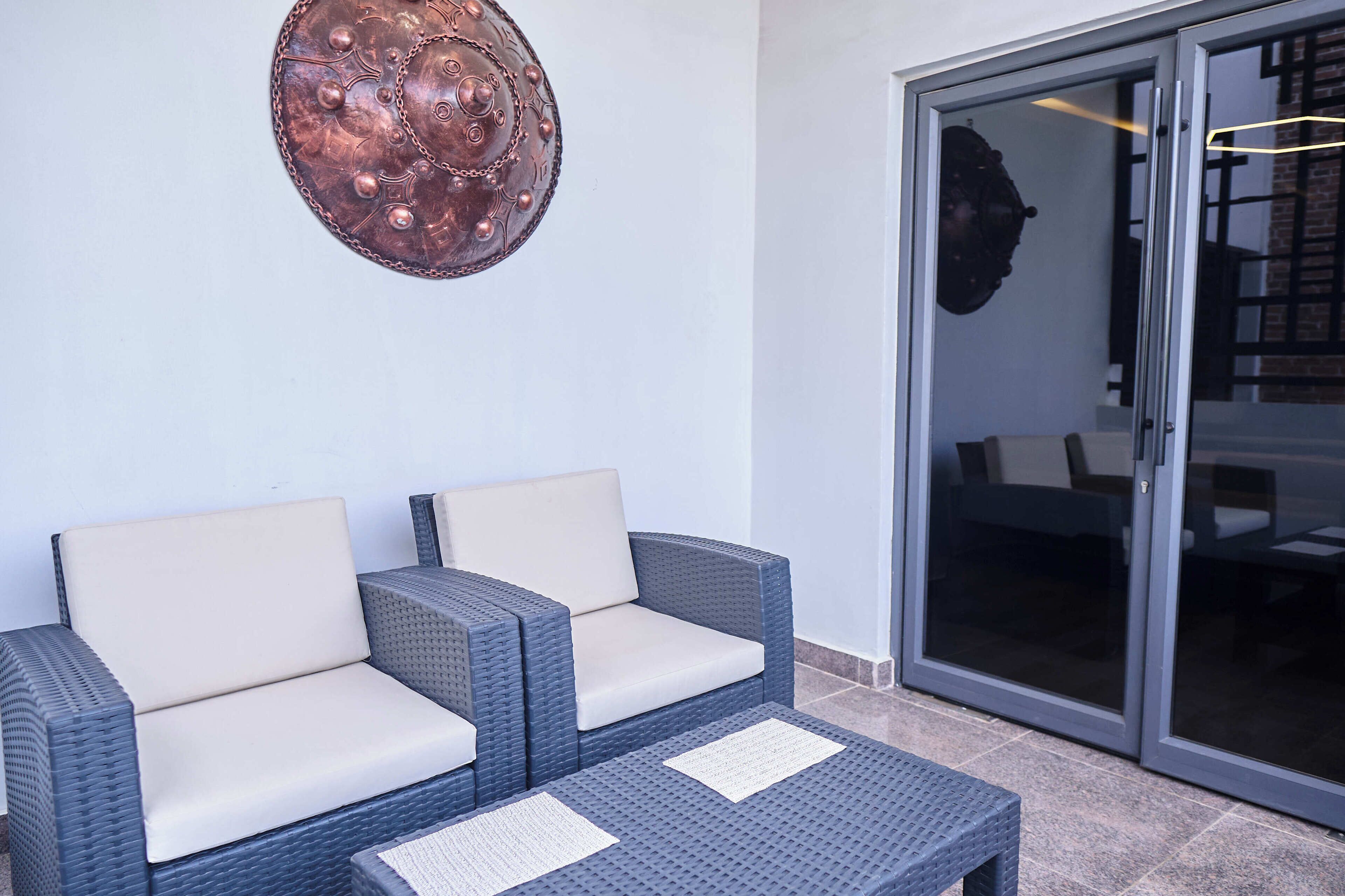 Un coin salon avec deux fauteuils confortables et une petite table, un élément décoratif mural, et une porte-fenêtre coulissante donnant sur un espace intérieur.