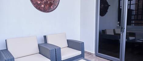 Un coin salon avec deux fauteuils confortables et une petite table, un élément décoratif mural, et une porte-fenêtre coulissante donnant sur un espace intérieur.