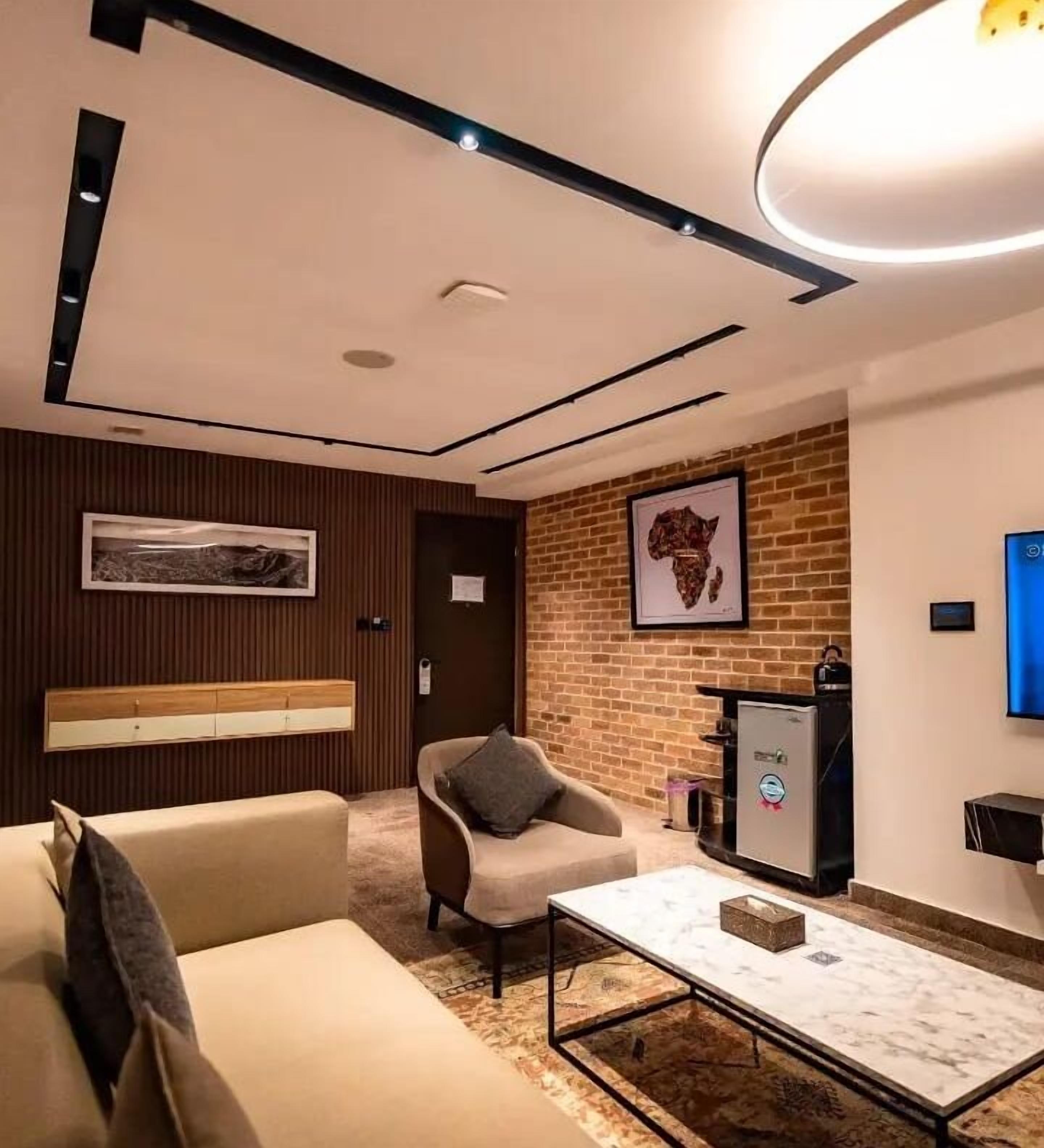A modern hotel room with a sofa, armchair, and a small table. There is a brick wall and a framed picture on the wall.