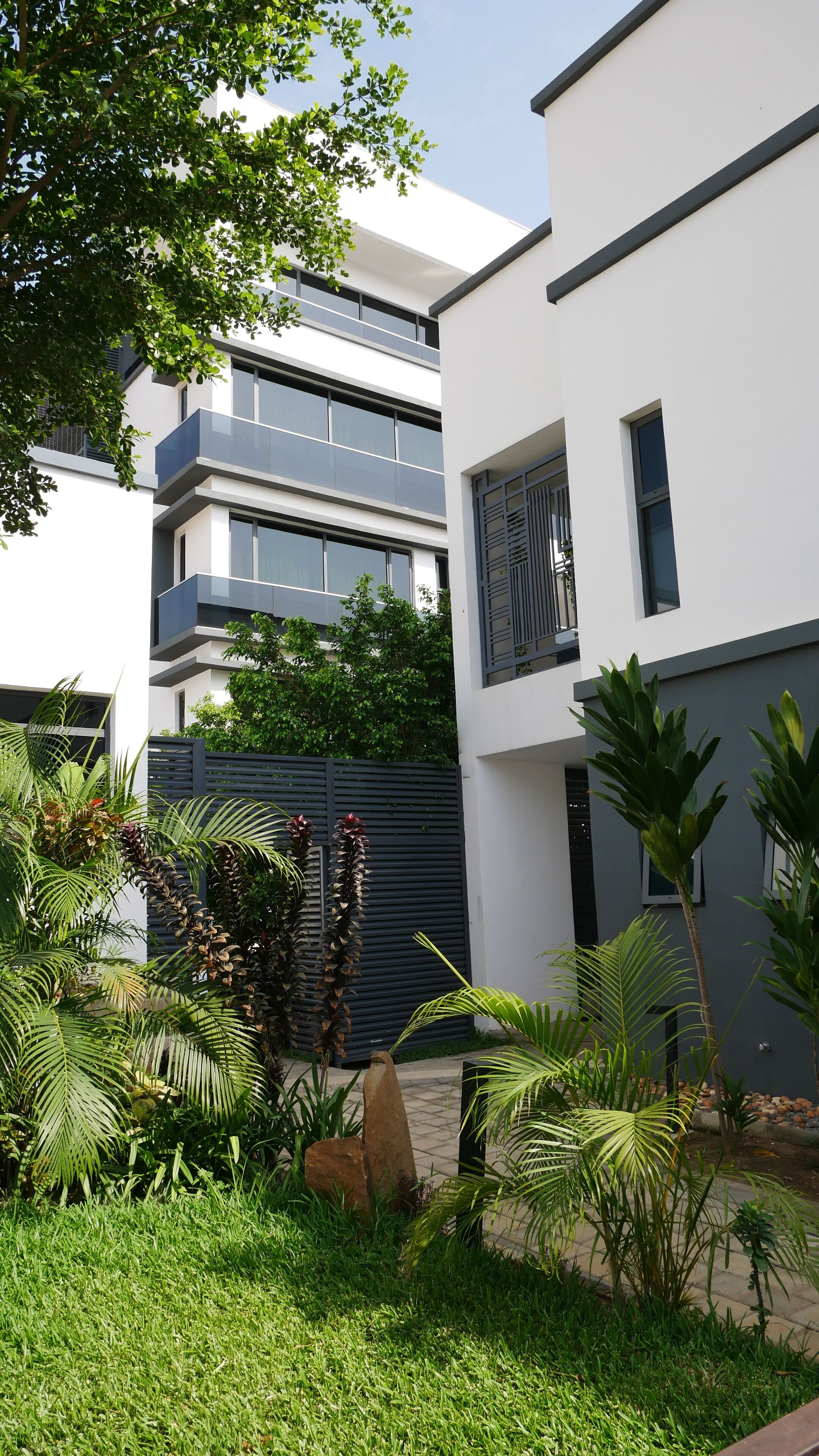 Een modern gebouw met een plat dak, grote ramen en een verzorgde tuin met verschillende planten en een rotsdecoratie.