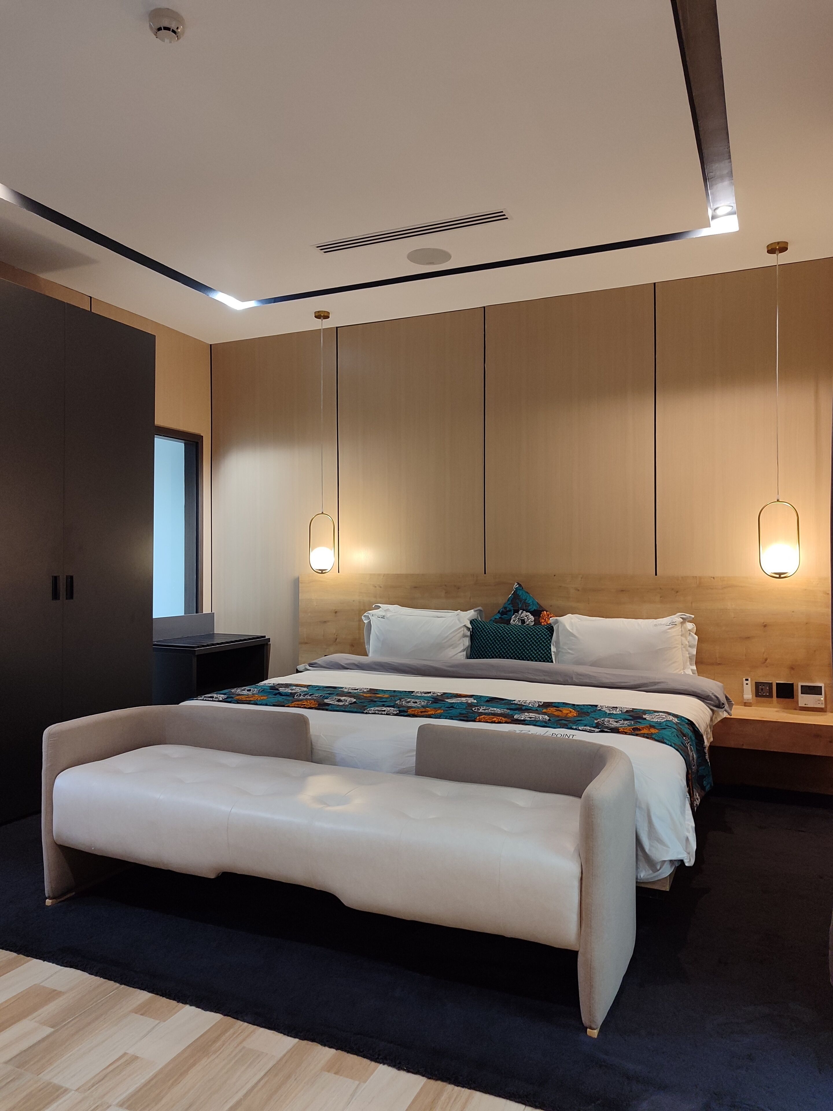 Une chambre d’hôtel moderne avec un grand lit, une table de chevet, un banc et une armoire.