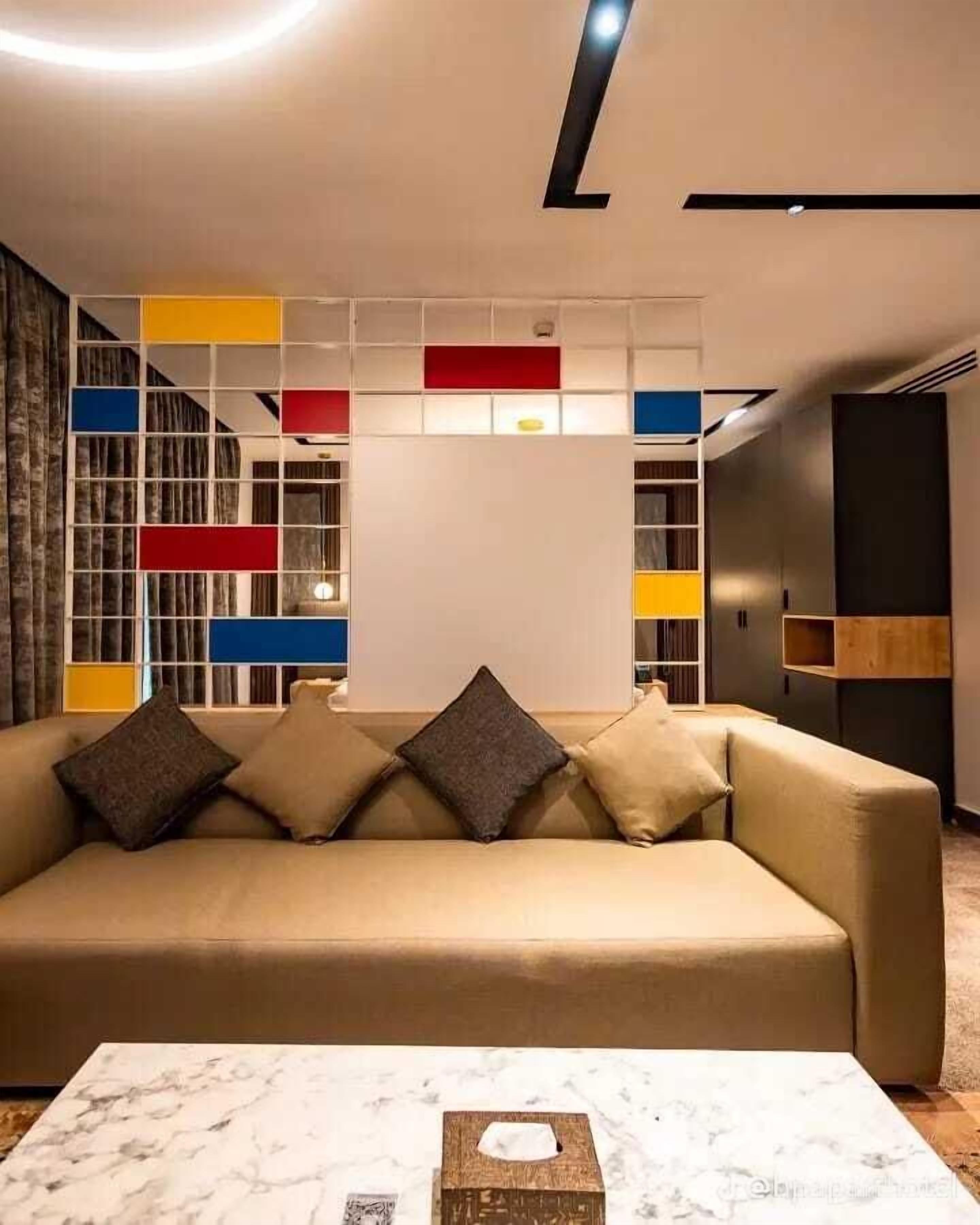 Ett modernt vardagsrum med en beige soffa, ett soffbord i marmor och en färgstark, abstrakt väggpanel.
