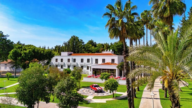 A white building with a red roof, surrounded by palm trees and a well-maintained lawn. - 74 Hotel (Antalya)