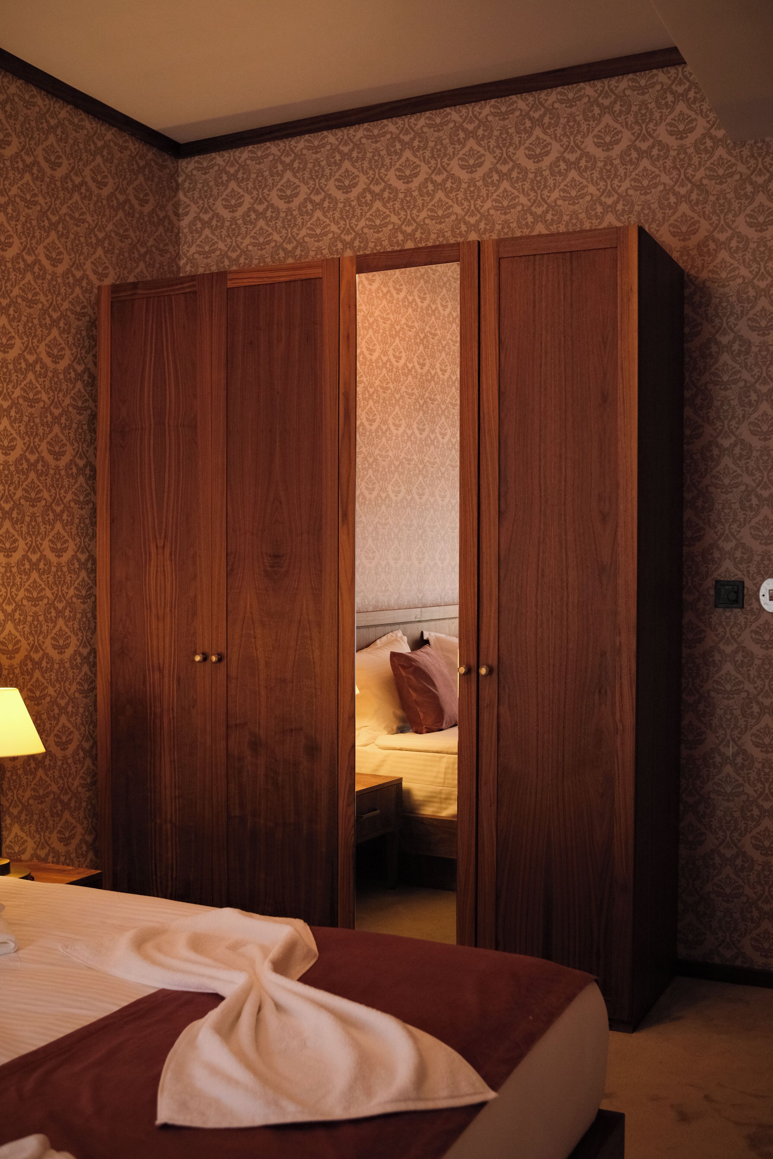 A bedroom with a bed, a wooden wardrobe, and a nightstand with a lamp.