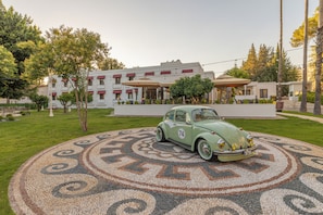 A vintage car parked on a patterned pavement in front of a building with a white facade and red awnings. - 74 Hotel (Antalya)