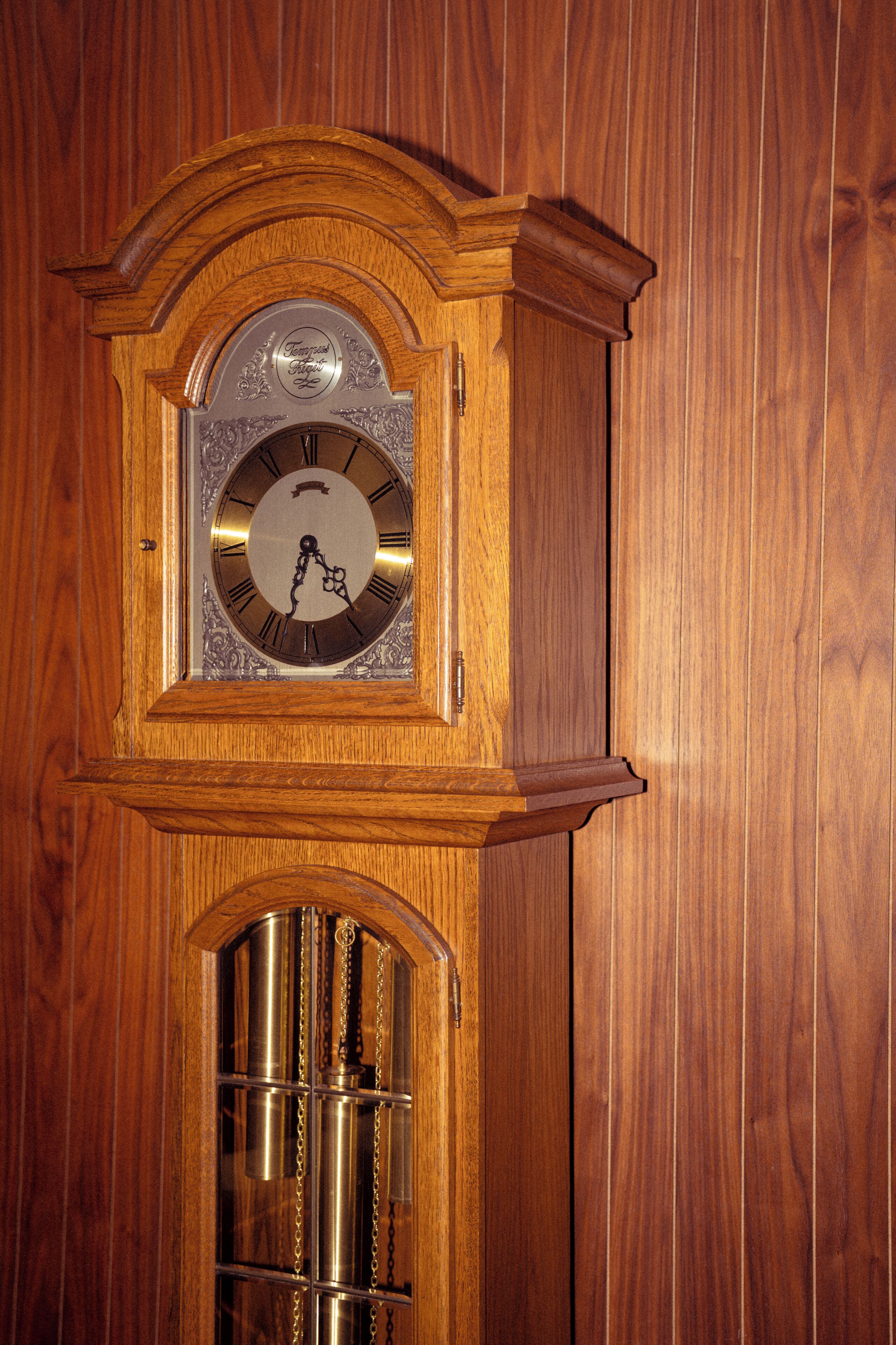 A wooden grandfather clock with a pendulum and a glass door.
