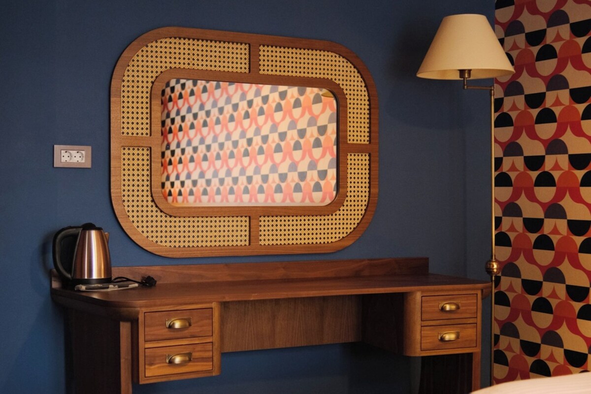 A bedroom with a bed, a wooden desk with drawers, a kettle, and a lamp.