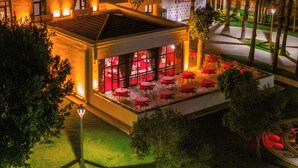 A hotel with a terrace featuring red tables and chairs, surrounded by trees and a well-lit interior. - 74 Hotel (Antalya)
