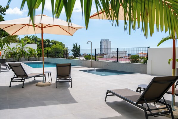 Relax by the rooftop pool with a stunning city view, surrounded by lush greenery and comfortable lounge seating.