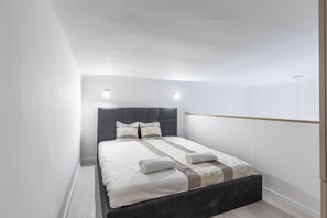 A modern bedroom with a dark headboard, white bedding, and a wooden shelf. - Lovely Apartment by National Museum (Budapest)