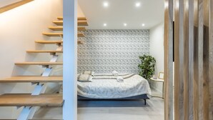 A modern bedroom with a geometric-patterned headboard, a bed with a leaf-patterned bedspread, and a wooden staircase. - Lovely Apartment by National Museum (Budapest)