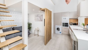 A modern kitchen with white appliances, a wooden staircase, and a grey sofa. - Lovely Apartment by National Museum (Budapest)