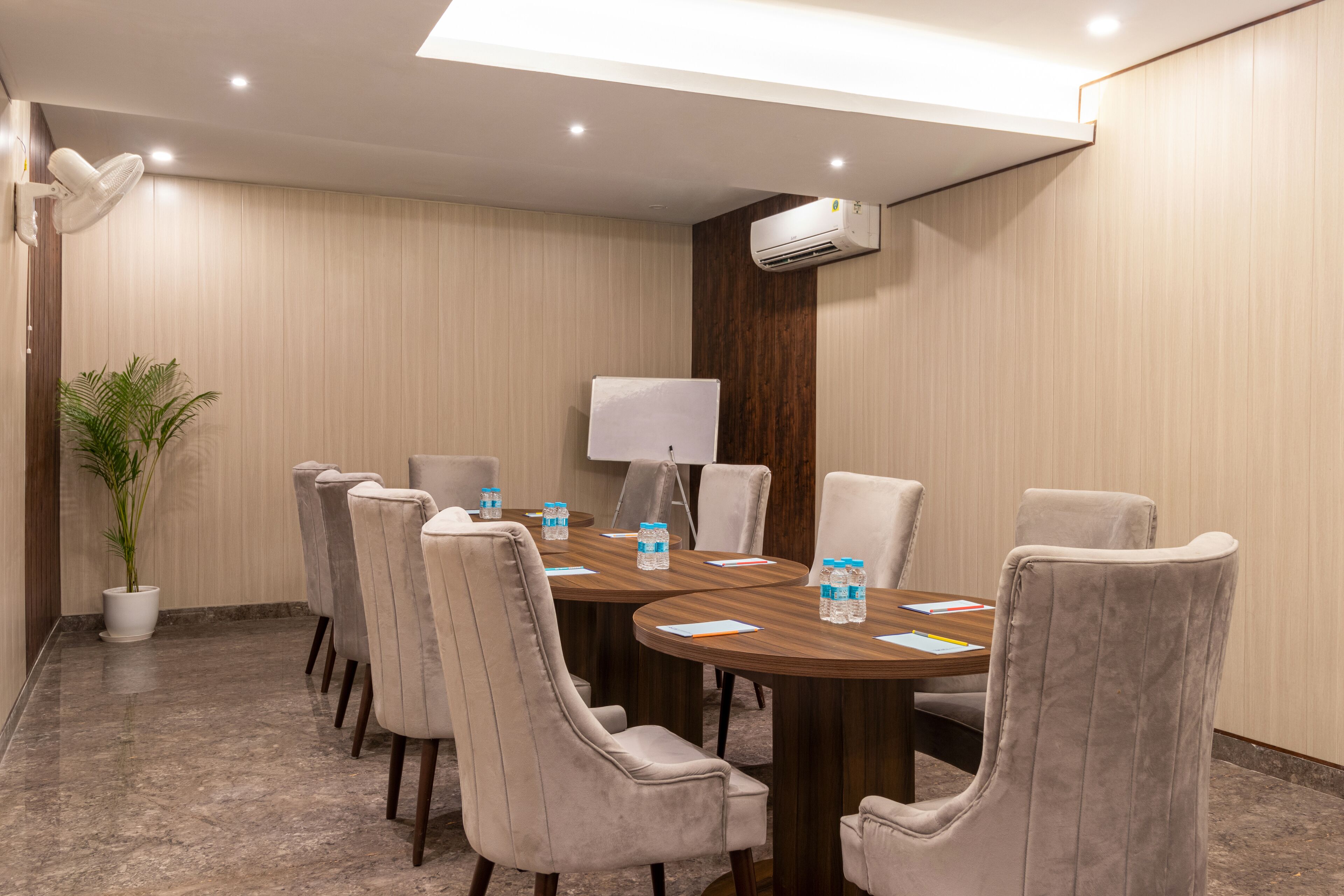 A conference room with a round table, six chairs, a potted plant, and an air conditioning unit.