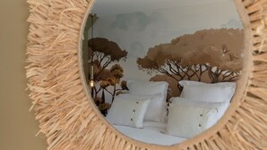 Een ronde spiegel met een reliëfomlijsting, die een kamer weerkaatst met een bed en een muurschildering.