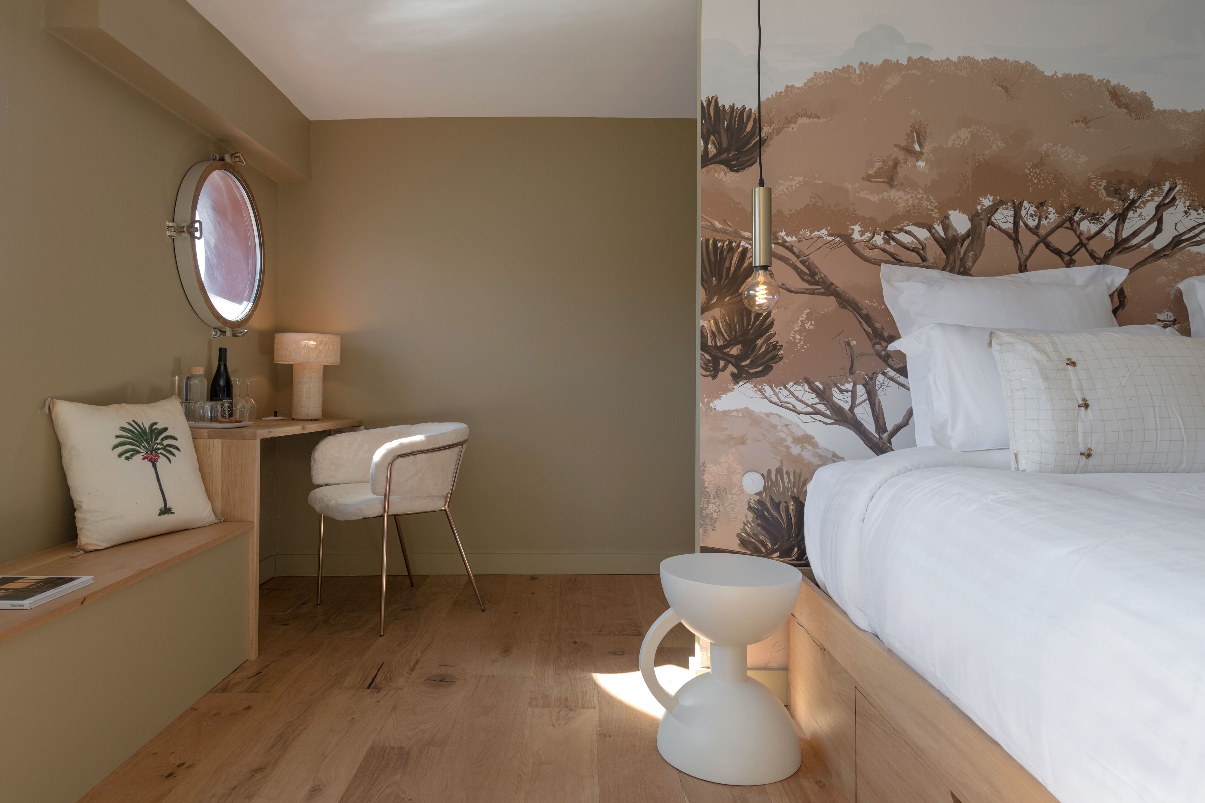A bedroom with a bed, a bedside table, a chair, a mirror, and a wall mural.