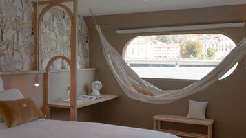 Quarto com uma cama grande, uma mesa de cabeceira de madeira, um banco e uma rede.