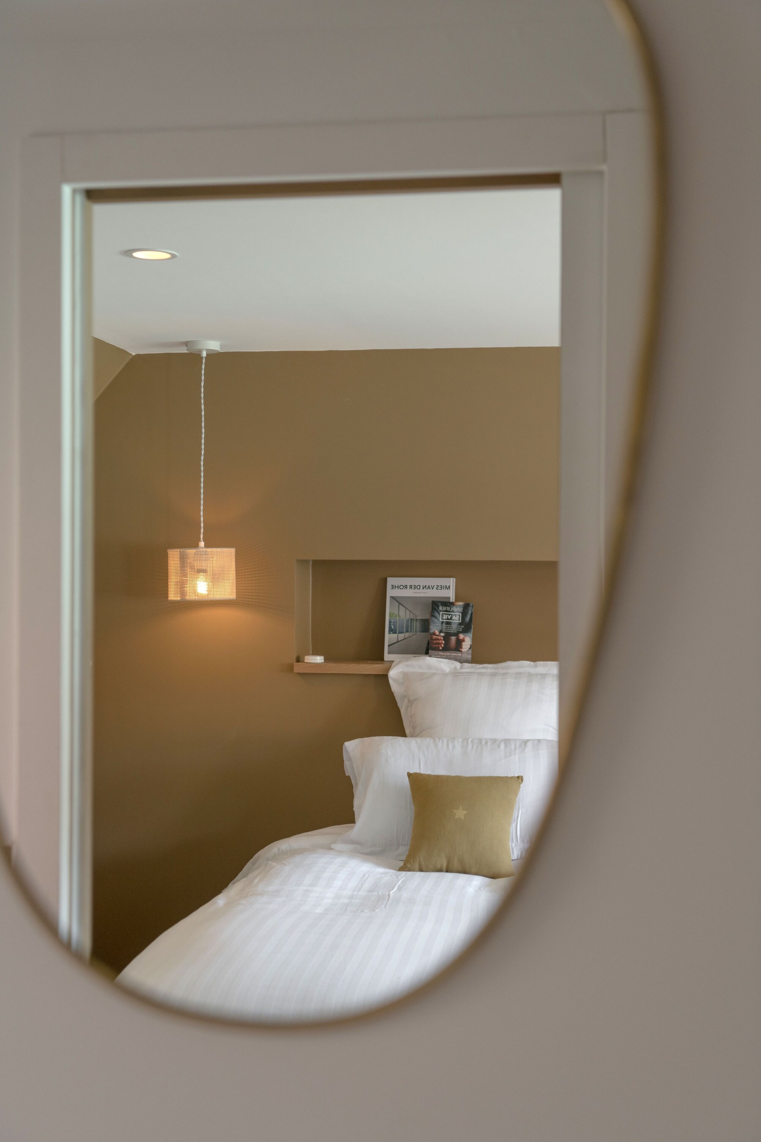 Een slaapkamer met een bed, nachtkastje, hanglamp en een wandplank met boeken.