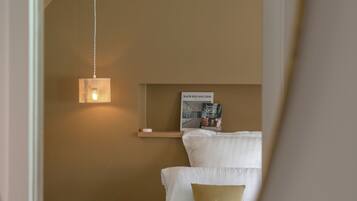 Een slaapkamer met een bed, nachtkastje, hanglamp en een wandplank met boeken.