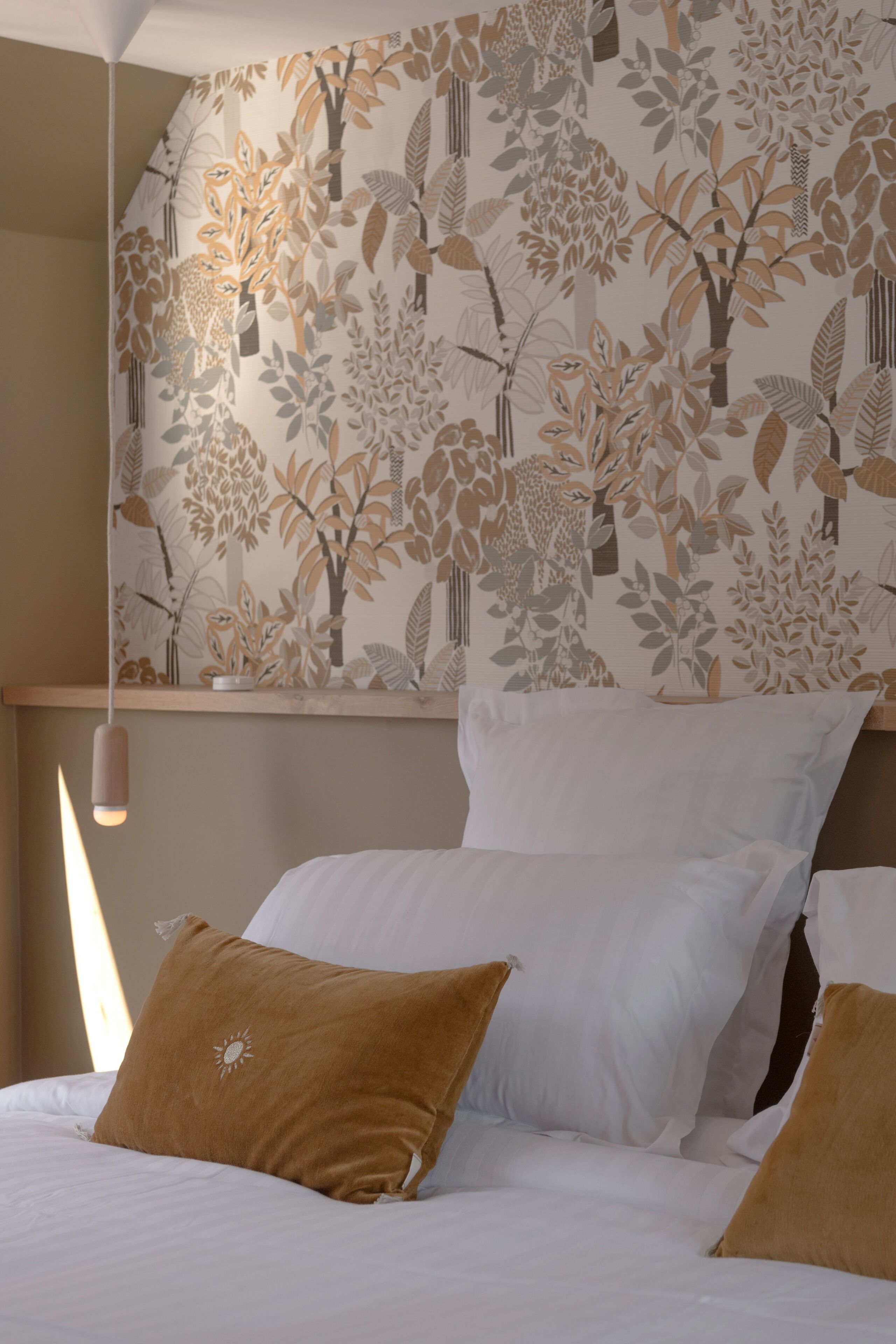 A bedroom with a bed, white and brown pillows, and a wall with a floral pattern.