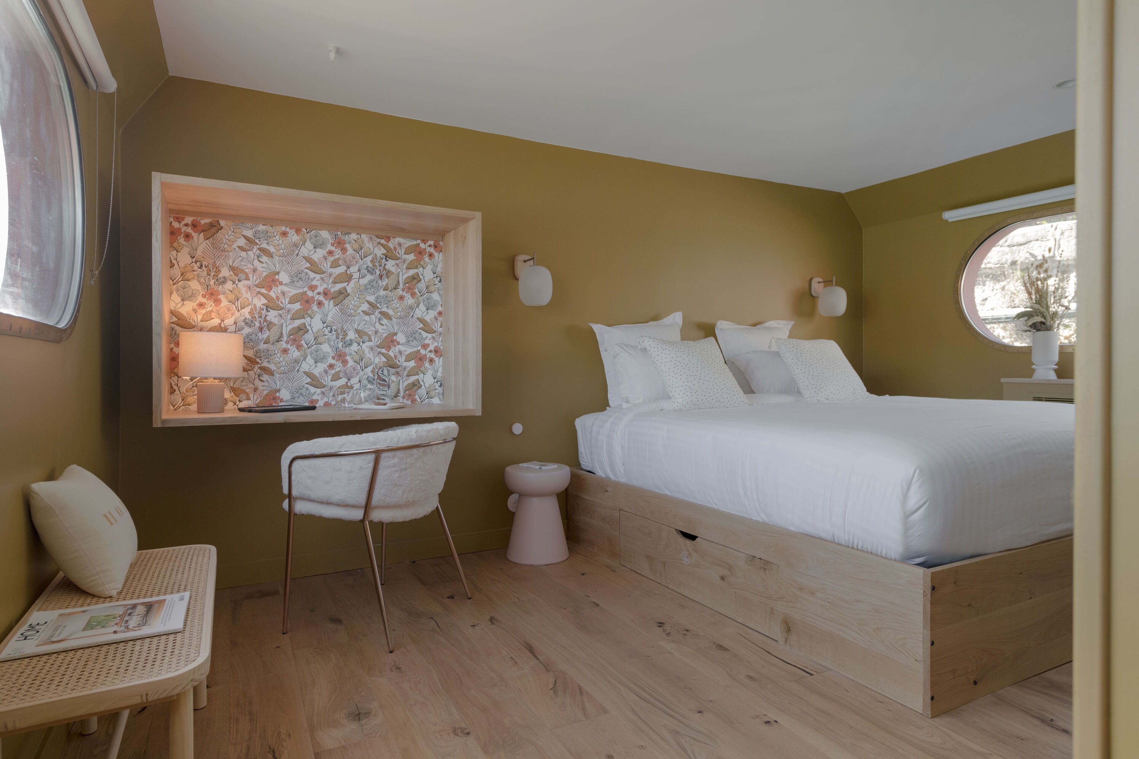 Un dormitorio con una cama de madera, una mesita de noche pequeña, una silla, una lámpara de pared y una ventana.