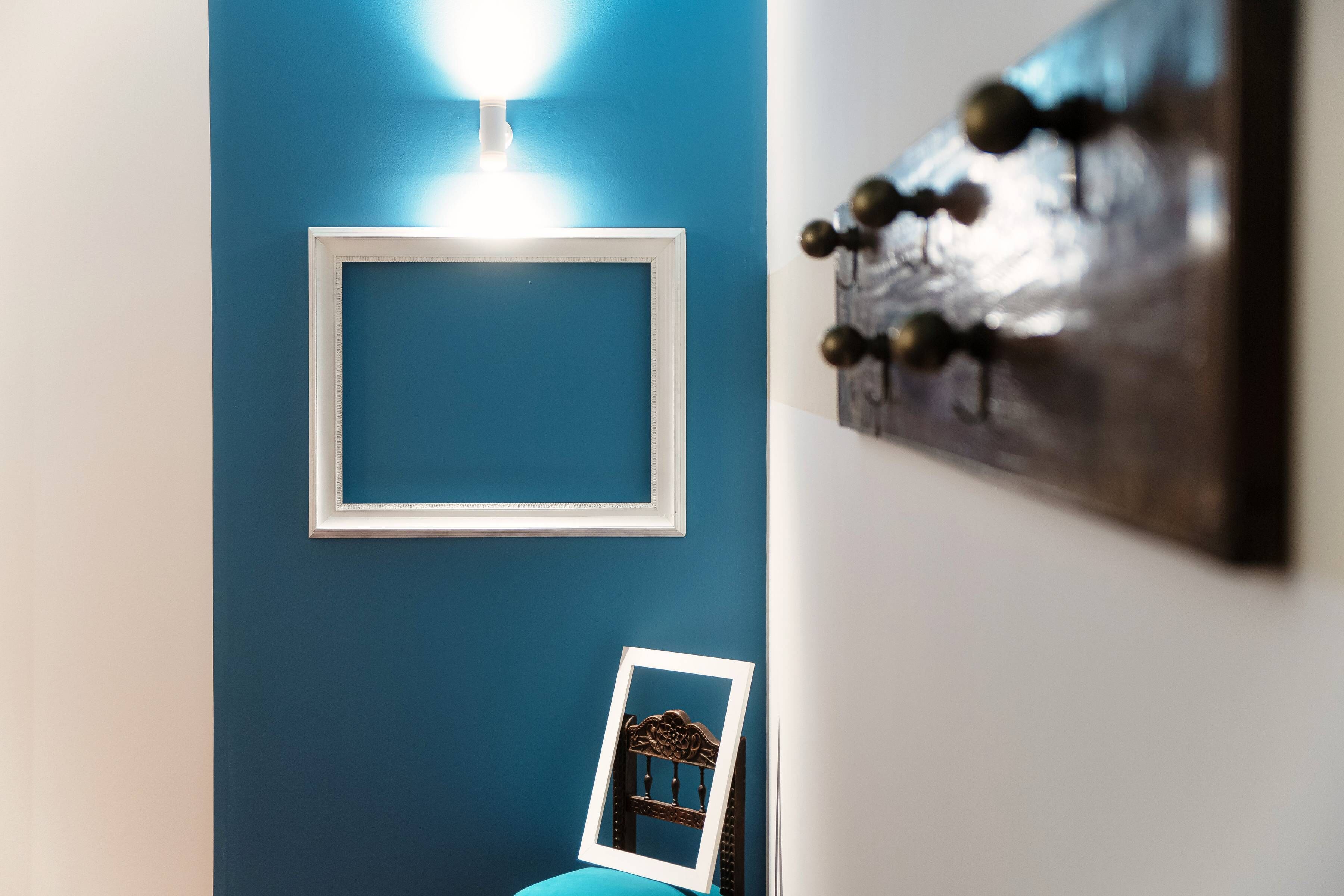 A room with a blue wall, a white-framed picture frame, and a wooden chair.